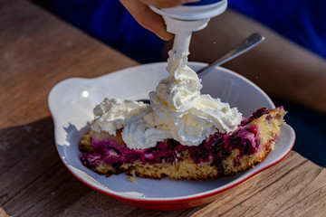 A man blows whipped cream on a berry cake at a garden table.
