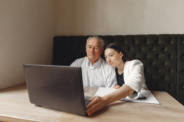 Senior with a young assistant. Businessman working in the cafe. Man in a white shirt. Young woman with her boss.