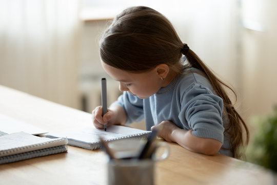 Small Girl Sit At Desk Writing In Notebook Studying Online Do Exercises At Home, Little Child Handwrite Prepare Homework On Quarantine, Have Web Class Or Lesson Indoors, Homeschooling Concept