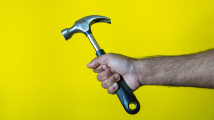 Male model holding hammer to fix home as a carpenter with yellow background