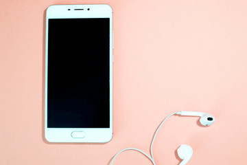 White phone with headphones on pink background