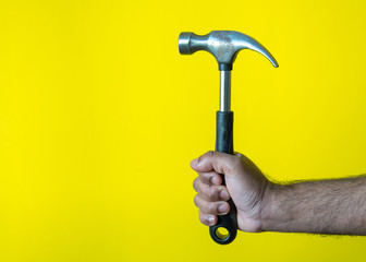 Male model holding hammer to fix home as a carpenter with yellow background