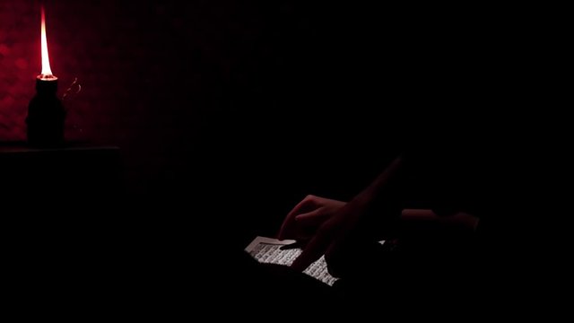 Muslim kid is learning to read The Quran in the dark room of rural house. Ramadan theme, or other Islamic spiritual events.
