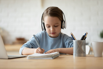 Cute little girl in headphones watch video tutorial drawing in album, small preschooler kid listen to music in earphones painting pictures, child studying online at home, homeschooling concept