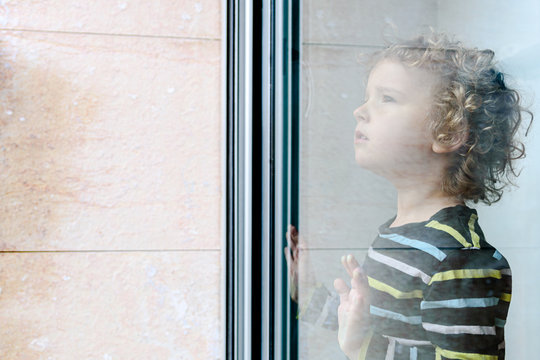 blonde little girl looks out the window during confinement