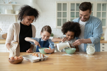 Happy young multiracial parents and little biracial daughters have fun baking in kitchen together,...