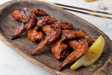 
BBQ chicken wings on a wooden plate with lemon and sesame seeds.
