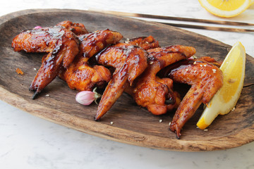 
BBQ chicken wings on a wooden plate with lemon and sesame seeds.