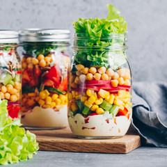 Fototapeta na wymiar Layering salad in a glass jar. Fresh radish, cucumber, celery, red bell pepper, corn, chickpeas and sauce.