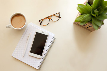 Mobile phone and notes paper. Retro style interior - cozy working place at home stylish interior in warm pastel colors, table and white coffee mug with glasses.stay home - a place for home office or a