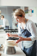 A middle aged woman pastry chef or baker prepares a cake and decorates it with icing.
