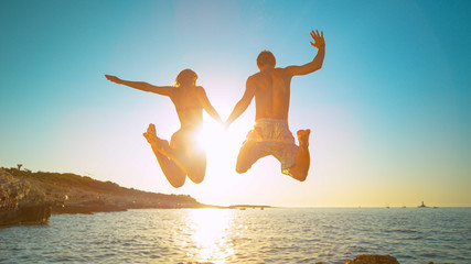 LENS FLARE: Carefree tourists hold hands while jumping into the refreshing sea