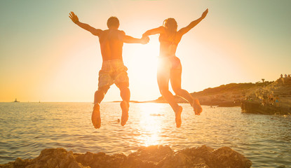 LENS FLARE: Golden sun rays shine on couple holding hands while diving into sea. - obrazy, fototapety, plakaty