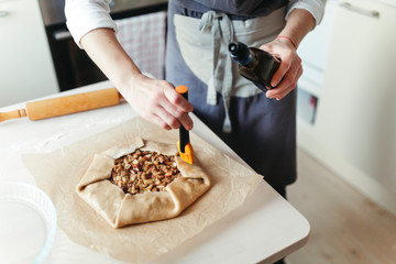 A woman in an apron prepares an apple pie at home kitchen.