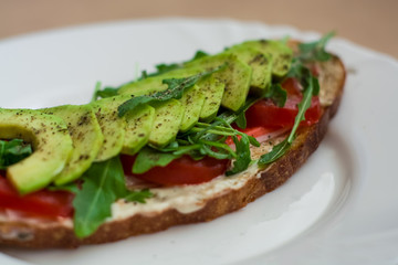 Fototapeta na wymiar Toast of dark bread, avocado with tomato and arugula. Healthy food, breakfast of fresh vegetables.
