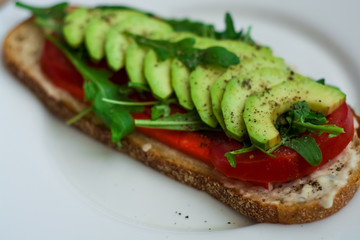 Toast of dark bread, avocado with tomato and arugula. Healthy food, breakfast of fresh vegetables.