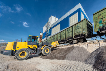 Wheel loader picks gravel in the bucket. Work on a flyover for unloading railway freight cars.