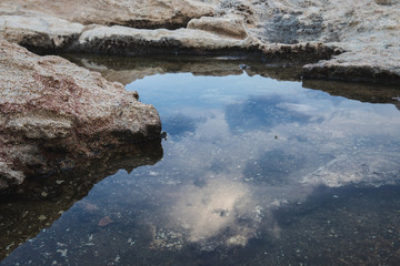rocky sea coast at sunset, waves breaking on the rocks, small pools formed by nature in the rocks with a reflection of the dark sunset sky before a thunderstorm