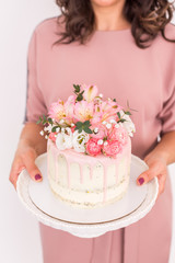 close up of women's hands holding a cake decorated with flowers on a white background