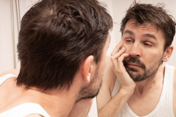 Obraz premium Sleepy shaggy young man looks at the mirror in bathroom in the morning.