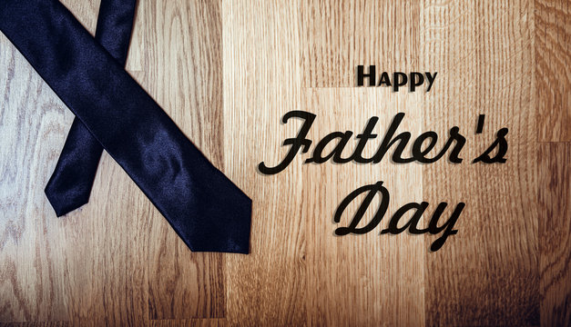 Happy fathers day sign on wooden background and black tie laid on. Minimal design concept.