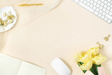 Stylized women's Desk, office Desk. Workspace with a computer, a bouquet of yellow tulips, clipboard. Women's fashion accessories on a light beige background. Flat top view