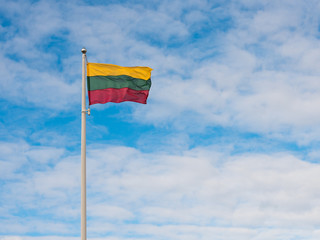 Lithuanian national flag on a pole in the background of blue cloudy sky
