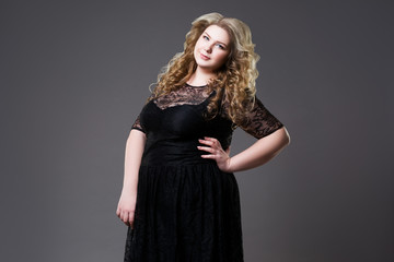 Plus size fashion model in black dress, fat woman on gray background