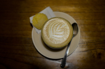 a glass of cappuccino and one biscuit on a wooden table

