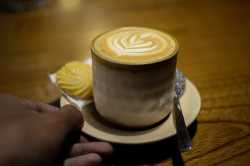 a glass of cappuccino and one biscuit on a wooden table
