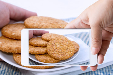 Woman hand holding smart phone take photo of homemade shortbread cookies made of oatmeal stacked in plate on cloth. Cooking recipes at the home kitchen. Cooking snack for food healthy concept.