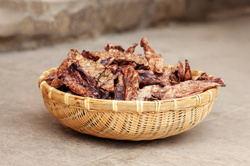 Dehydrated homemade pet beef lungs chips in straw pot on stone background. Dog and cat chewy jerky and treats. Outdoors, close up, soft selective focus, copy space.