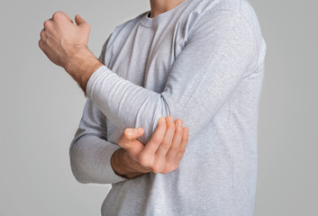 Man touches painful elbow on grey background