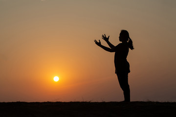 Silhouette of woman standing with arms raised on mountain