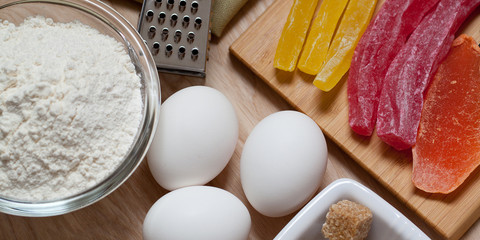 three eggs, flour and dried fruit are prepared for baking on a wooden surface