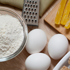 three eggs, flour and dried fruit are prepared on a wooden surface for home baking