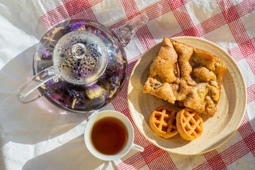 Glass teapot with fruit tea and cookies on a tablecloth on the background of a summer beach with sand and water