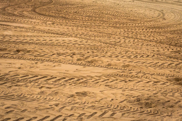 Naklejka premium Tire tread on the sand. Wet sand on the beach. Background for screensaver. Footprints in the sand. Sandy background. Leave traces. Unsteady road. Riding on a sandy surface.