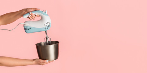 Closeup of young woman holding electric mixer and bowl on pink background, empty space. Panorama