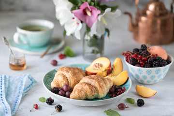 Breakfast of fresh berries and fruits with croissants, teas a bouquet of summer flowers.