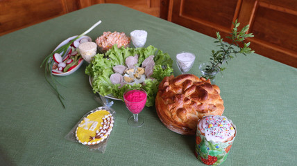 Holiday table covered with a green tablecloth, with appetizer, salads, Easter cake, honey gingerbread with icing