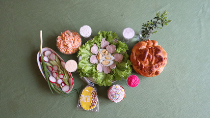Holiday table covered with a green tablecloth, with appetizer, salads, Easter cake, honey gingerbread with icing