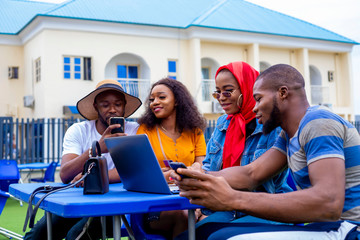young black friends sitting out, having fun and using a laptop