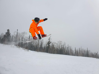 Jumping snowboarder keeps one hand on the snowboard on blue sky background