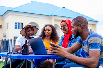 young black friends sitting out, having fun and using a laptop