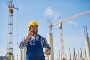 An engineer uses radio set on his work place with a folded draft.
