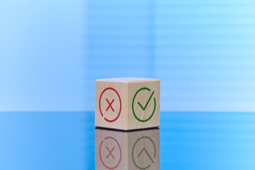 The concept of making the right choice and decision. The blue background shows a wooden cube with a reflection on the surface, on the side faces of the image of a positive and negative choice.