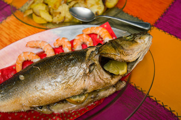 cooked sea bass on a glass dish and a plate with baked potato garnish