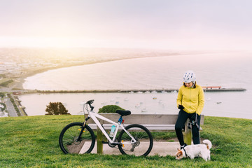 Asian woman making uphill with mountain bike. A woman taking a picture at lookout point with a dog at Oamaru, New Zealand.