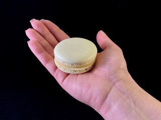 Multicolored tasty macarons on a black background. Colorful french macarons of various tastes, top view. Dessert in the hand, exquisite taste.